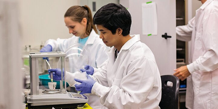 Students in lab coats working in lab.